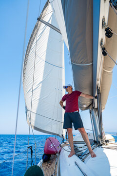 Experienced sailor standing beside the mainsail on a sailing yacht during an offshore passage. Confidence, seamanship, active cruising lifestyle and wind powered navigation at sea.