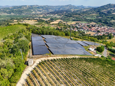 Aerial view of a solar power plant installed on a hilltop, replacing a vineyard with rows of vines and surrounding rural landscape in Monastero Bormida, Piedmont, Italy.