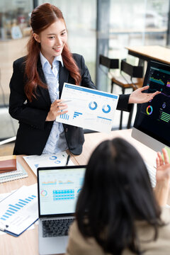 Asian Business Woman Presenting Financial Paper Report and Gesturing to Computer Screen