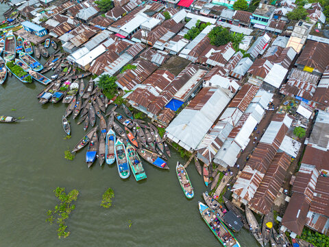 Aerial view of Baithakhata Bazar featuring a riverfront market with wooden boats moored along the bank and rows of metal rooftops in Kolardoania Union, Barisal Division, Bangladesh.