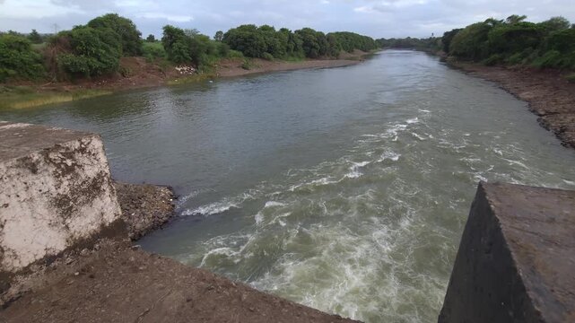 Observation of a stone training wall altering the course of turbulent river rapids as they surge into the open channel, conceptualizing river engineering, flow velocity control, and bank defense.