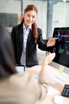 Asian Business Woman Pointing Stylus at Computer Screen Presenting Data to Client