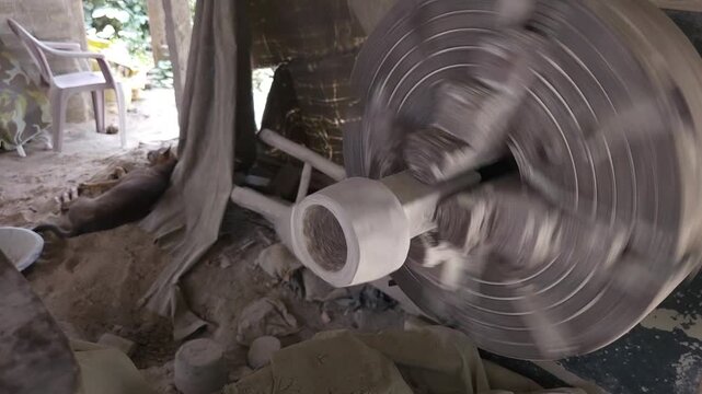 Slow-motion horizontal footage of an Indian artisan shaping a granite stone utensil on a rotating lathe machine. The spinning stone is carefully worked with cutting tools to create a rounded form