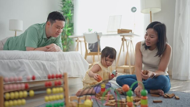 Cheerful kid girl playing with colorful toys with loving parents in house. 