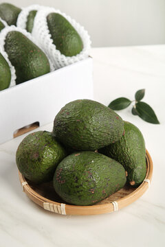 Fresh Mexican avocados in wicker basket on white table with natural lighting