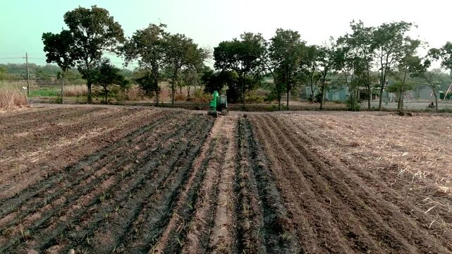 Drone footage showing an aerial view of agricultural fields, including harvested sugarcane and pomelo orange orchards, with heavy machinery parked near a rural road.