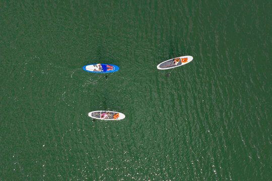 Aerial view of three people paddleboarding on the green water of the Pacific Ocean at Huntington Beach, California, United States.