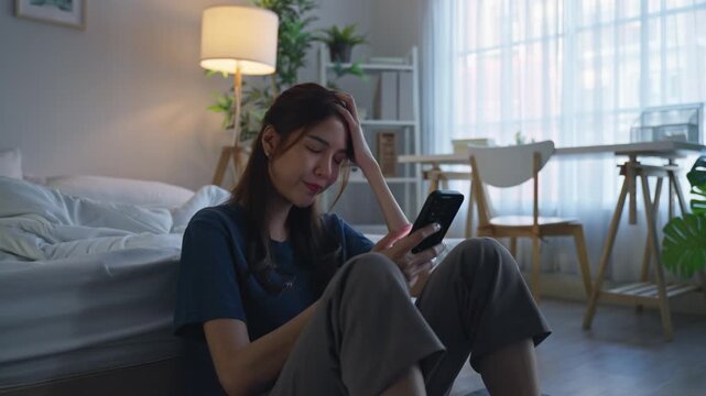 Asian young depressed woman looking at mobile phone in bedroom at home. 