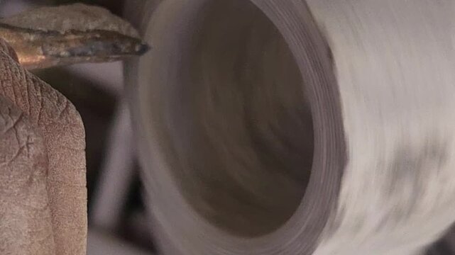 Slow-motion horizontal footage of an Indian artisan shaping a granite stone utensil on a rotating lathe machine. The spinning stone is carefully worked with cutting tools to create a rounded form