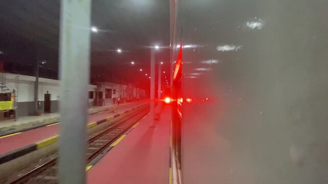 Side view of a passenger train with bright red signal lights reflection at an empty station platform at night