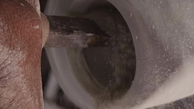 Slow-motion horizontal footage of an Indian artisan shaping a granite stone utensil on a rotating lathe machine. The spinning stone is carefully worked with cutting tools to create a rounded form