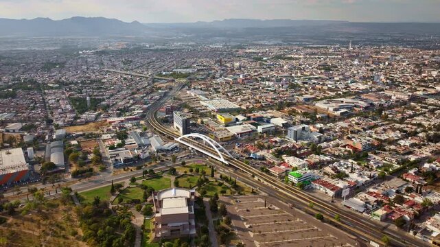 Wide aerial timelapse showing everyday urban activity in Aguascalientes, with Avenida Aguascalientes Sur extending toward the horizon and the Bicentenario Bridge centered below.