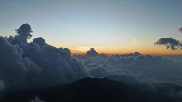 Aerial view of sunset over cloud inversion above mountainous terrain near Telaga Dringo in Kecamatan Batur, Jawa Tengah, Indonesia.