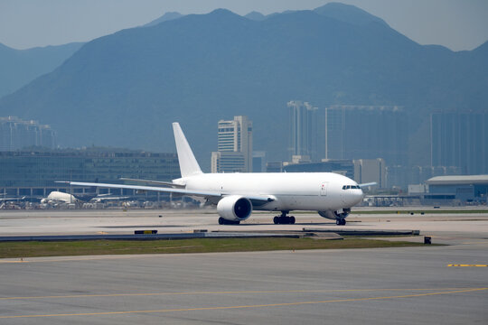 Large cargo airplane taxis on the runway, ready to ascend into the clear sky, surrounded by majestic mountains and modern city buildings