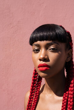 Woman with red braided hair and bold makeup against pink background