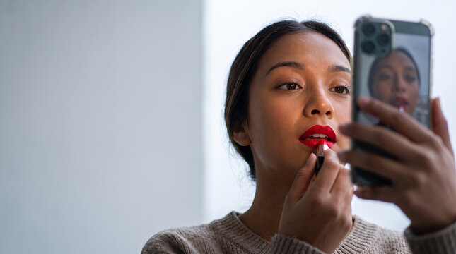 Woman applying red lipstick while taking selfie with smartphone