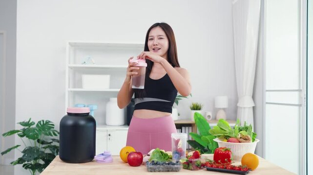 Energetic young female live streaming plant-based diet tutorial using smartphone. Asian wellness vlogger showing fresh vegetables for healthy sports nutrition and vitality.