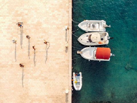 Aerial view of people walking on a stone pier next to moored boats in the clear blue water of the Adriatic Sea in Brela, Split-Dalmatia County, Croatia.