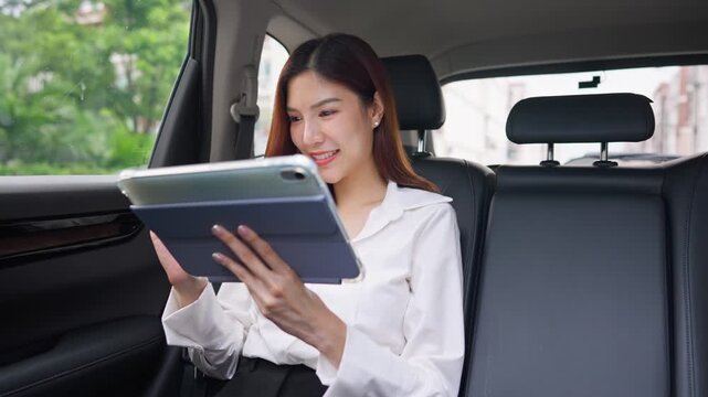 Asian woman using digital tablet while sitting in the back seat of a car. 