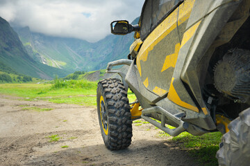 Close up of a yellow dirty offroad UTV buggy car parked on a dirt trail looking towards a majestic green mountain valley under a cloudy sky. Extreme motorsport travel adventure concept design © GIS