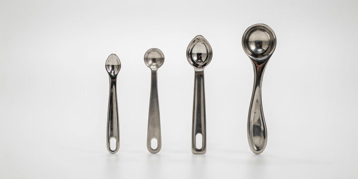 Four stainless steel measuring spoons of different sizes on white