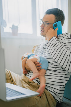 Father balancing a baby in one arm while working on a laptop and talking on a phone, representing the challenges and flexibility of remote work, paternity leave, and modern parenthood