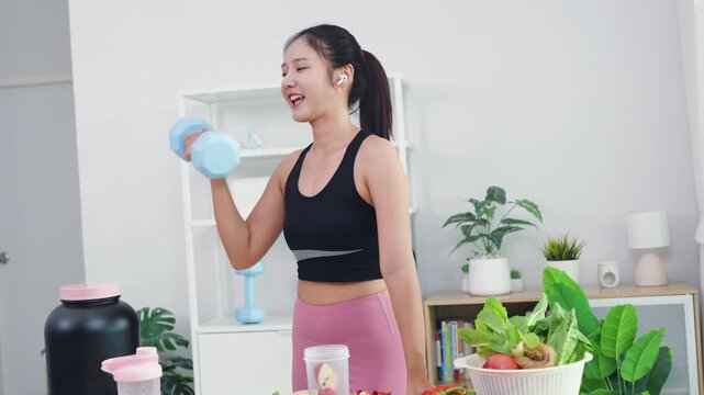 Vibrant Asian fitness vlogger making healthy juice tutorial video in home kitchen. Happy female influencer talking to smartphone camera about nutrition and active lifestyle.