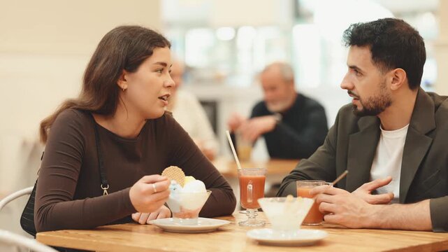 Woman and a man at a table in a cafe, they enjoys dessert and drinks. Young couple chatting in a coffee shop. High quality 4k footage