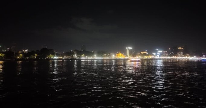 Night view of Phnom Penh skyline featuring the illuminated Royal Palace and a cruise boat on the Tonle Sap, seen from a boat.