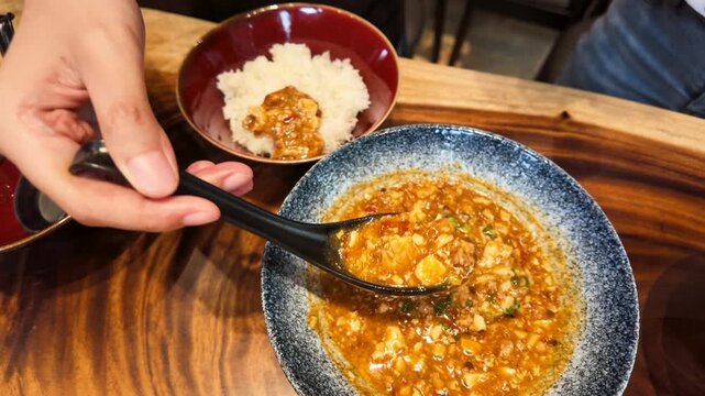 Spoon Scooping Spicy Mapo Tofu onto White Rice in Bowl