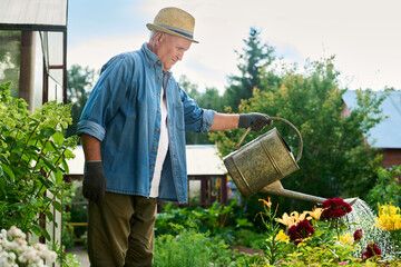 Senior Caucasian man watering flowers with metal can in garden, representing active retirement and...