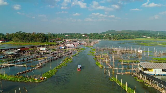 Aerial view of Lake Rawa Pening with traditional fish farms and a small boat navigating the water in Waduk Rawapening, Central Java, Indonesia.