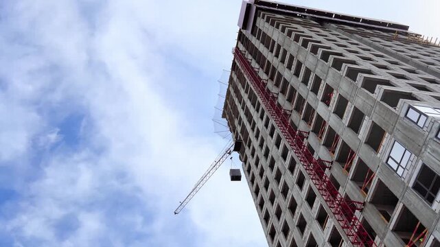 Upward view of tower crane beside high rise building under clouds