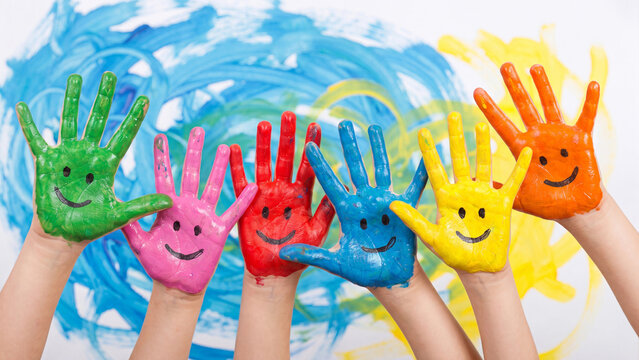 Children's hands painted with colorful faces raised in a row express joy, creativity, and artistic play during an elementary school art class session.