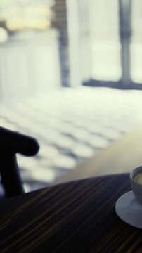 A delightful coffee cup sits on a wooden table, bathed in warm sunlight. Shadows dance playfully across the floor, creating a welcoming atmosphere in this inviting cafe setting.