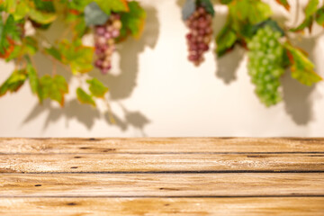 Fototapeta premium Wooden table with blurred grape bunches and vine leaves as autumn harvest mockup background