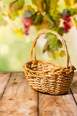 Naklejka premium Wicker basket on wooden table with blurred grapevine background for rustic autumn harvest product scene