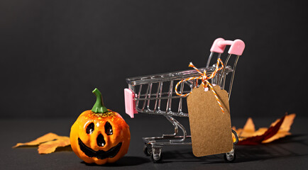 Jack-o-lantern and shopping cart with hanging blank tag on dark background for Halloween sale banner or retail mockup © Svetlana Kolpakova