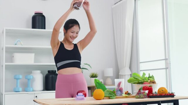 Fit Asian woman recording healthy diet and sports nutrition vlog in home kitchen. Active female content creator sharing organic food preparation and wellness supplement advice for vitality.