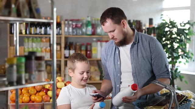 European man with son customer at shop scan QR code on milk bottle using phone camera. Client study composition, manufacturer information of product using application. Visitor examines product