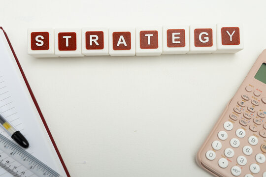 Business organization and administration concept featuring letter blocks spelling &ldquo;STRATEGY&rdquo; on a clean office desk, surrounded by office stationaries.