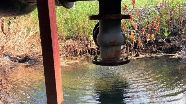 Weathered metal pipe valve stands over shallow water in abandoned area
