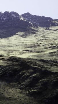 Rocky peaks rise dramatically in the distance, cloaked in snow, while gentle hills roll gracefully in the foreground. Nature awakens under the warm glow of afternoon light.