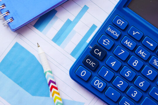 Blue calculator placed on financial bar chart reports for accounting and tax calculation tasks with calculator
