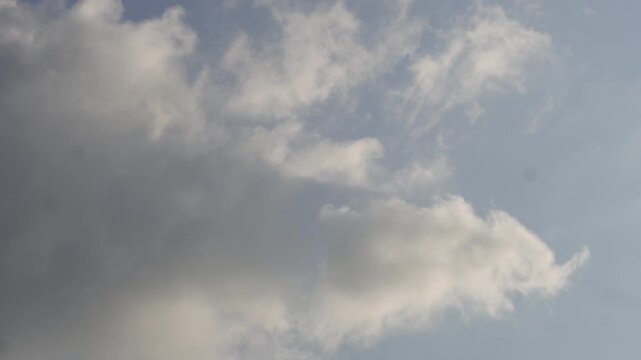 Soft cumulus clouds drifting across pale blue sky