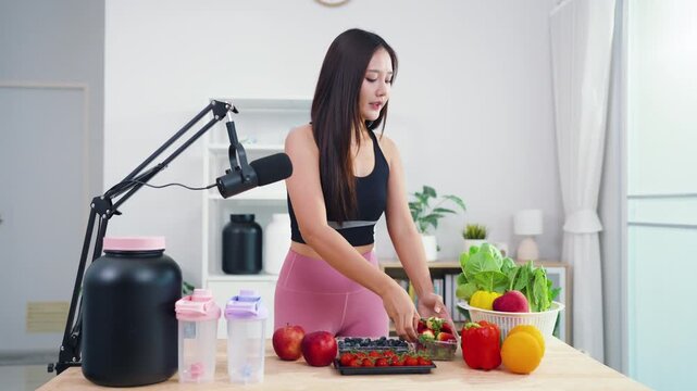 Asian fitness influencer recording healthy nutrition vlog with smartphone camera. Young female content creator talking about diet, fresh organic food and wellness lifestyle.