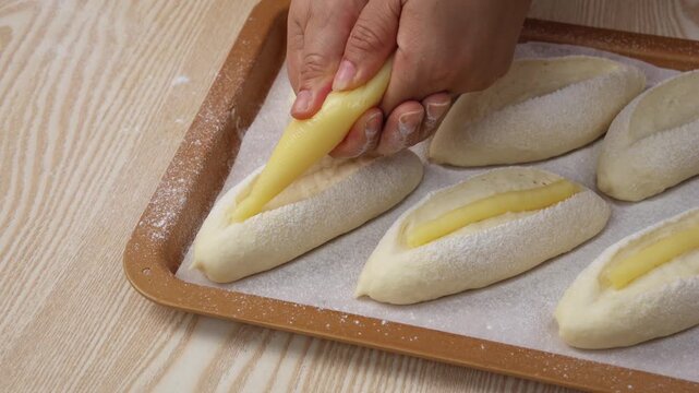 Baker Piping Cream Filling Onto Fresh Dough Buns on Baking Sheet