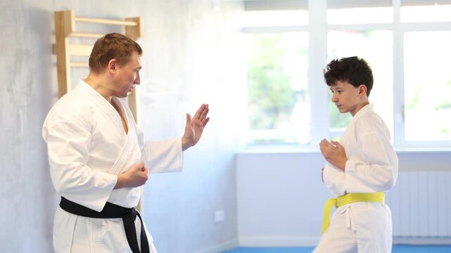 Adult man and teenage boy karatekas training karate fight in studio