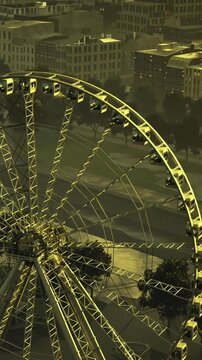 The ferris wheel rises elegantly against the urban skyline, illuminated in golden hues. As evening falls, the city buzzes with life below, making the scene enchanting and vibrant.