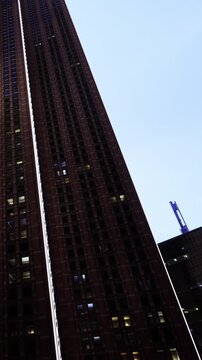 Tall buildings stand majestically as dusk settles over the city. Lights flicker on, casting a warm glow against the evening backdrop. The atmosphere buzzes with life and energy.